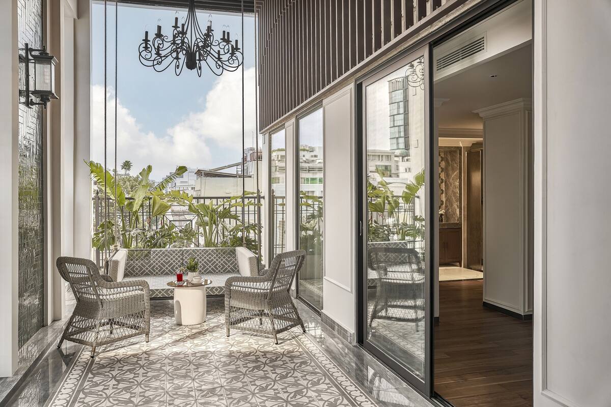 Ein Balkon mit Korbmöbeln, einer Chandelüster und Blick auf die Stadt.