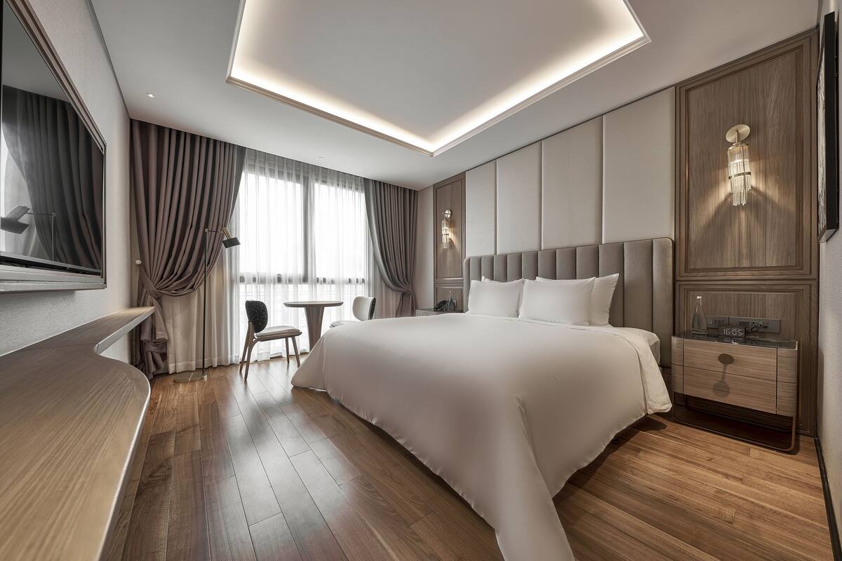 Ein modernes Hotelzimmer mit einem großen Bett, einem Nachttisch, einem Schreibtisch und einem Sessel.
