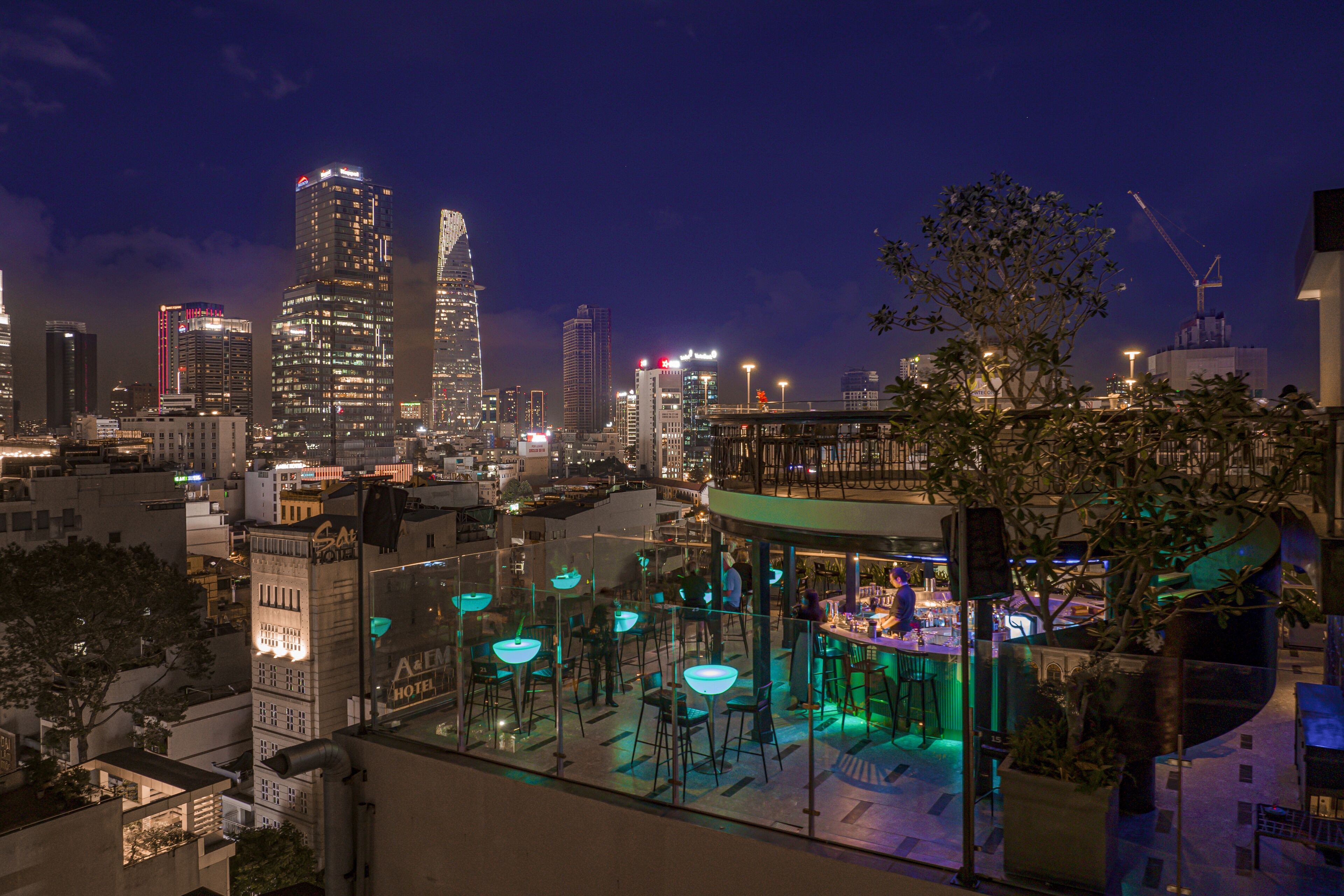 A rooftop bar with outdoor seating and a view of the city skyline at night.