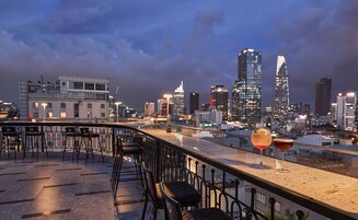 A rooftop bar with a city skyline view, bar stools, and two glasses of drink.