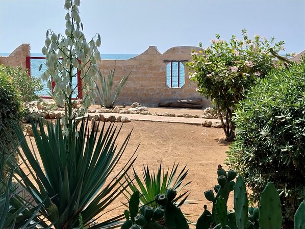 A courtyard with a view of the sea, surrounded by stone walls and various plants.