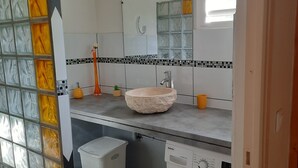 Ett badrum med en stor spegel, ett handfat med en beige tvättställsskål, en tandborsthållare och en liten krukväxt.
