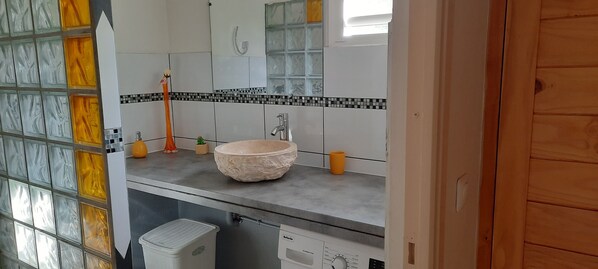 A bathroom with a large mirror, a sink with a beige basin, a toothbrush holder, and a small potted plant.