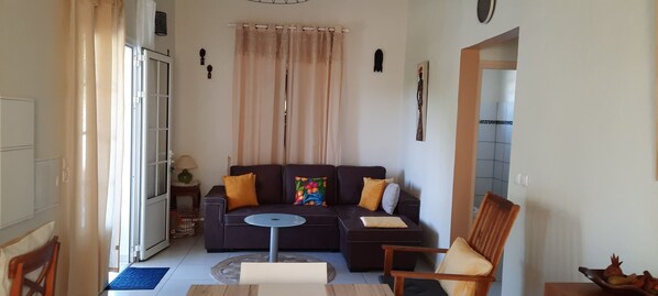 A living room with a dark brown sofa, a small round table, a wooden chair, and a glass door leading outside. - equipped villa near the beach (Petit-canal)