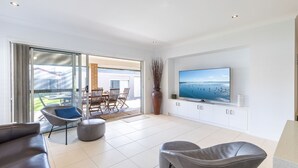 Un soggiorno moderno con una grande TV, sedute confortevoli e una porta vetrata scorrevole che dà su un'area pranzo all'aperto.