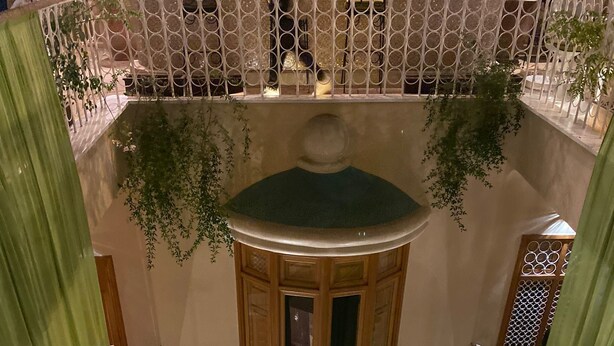 Un espacio interior de varios niveles con una fuente central, mesas y sillas dispuestas alrededor.
