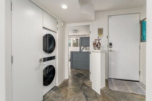 A laundry room with two front-loading washing machines, a grey door, and a small window.