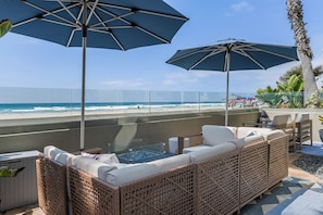 A beachside lounge with wicker furniture, a hot tub, and umbrellas providing shade.