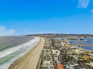 A coastal town with a long sandy beach, a marina with boats, and residential buildings along the shore.