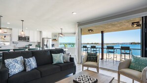 Un salon moderne avec un canapé noir, une table basse en bois et une vue sur la plage grâce à de grandes portes coulissantes.