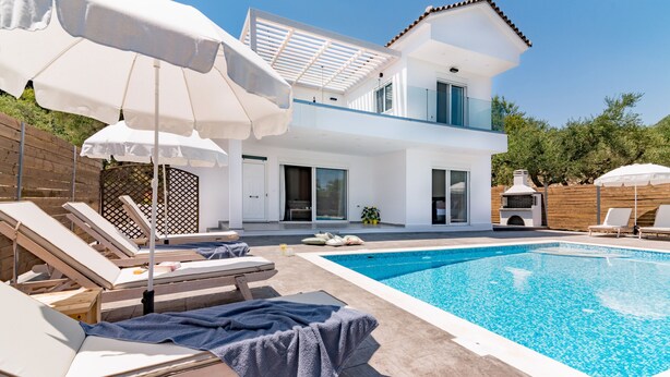 A modern two-story house with a swimming pool, sun loungers, and umbrellas.