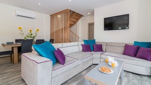 A modern living room with a sectional sofa, a coffee table with snacks, a TV mounted on the wall, and a staircase with wooden railings.
