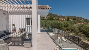 A modern outdoor patio with a glass balustrade, wicker furniture, and a pool.