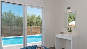 A bedroom with a sliding glass door leading to a pool, a white desk, and a mirror on the wall.