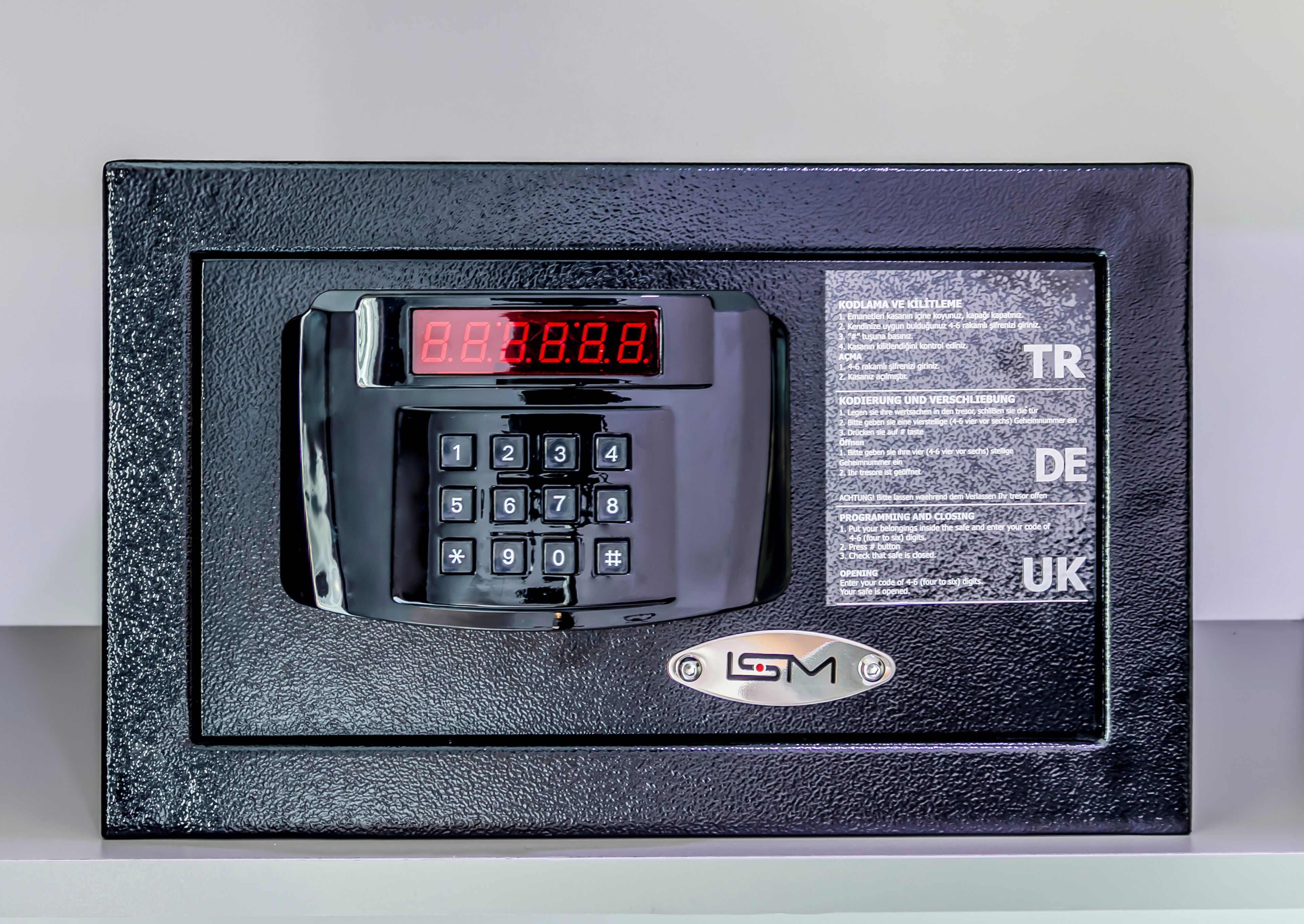A black security keypad with a digital display and instructions in multiple languages.