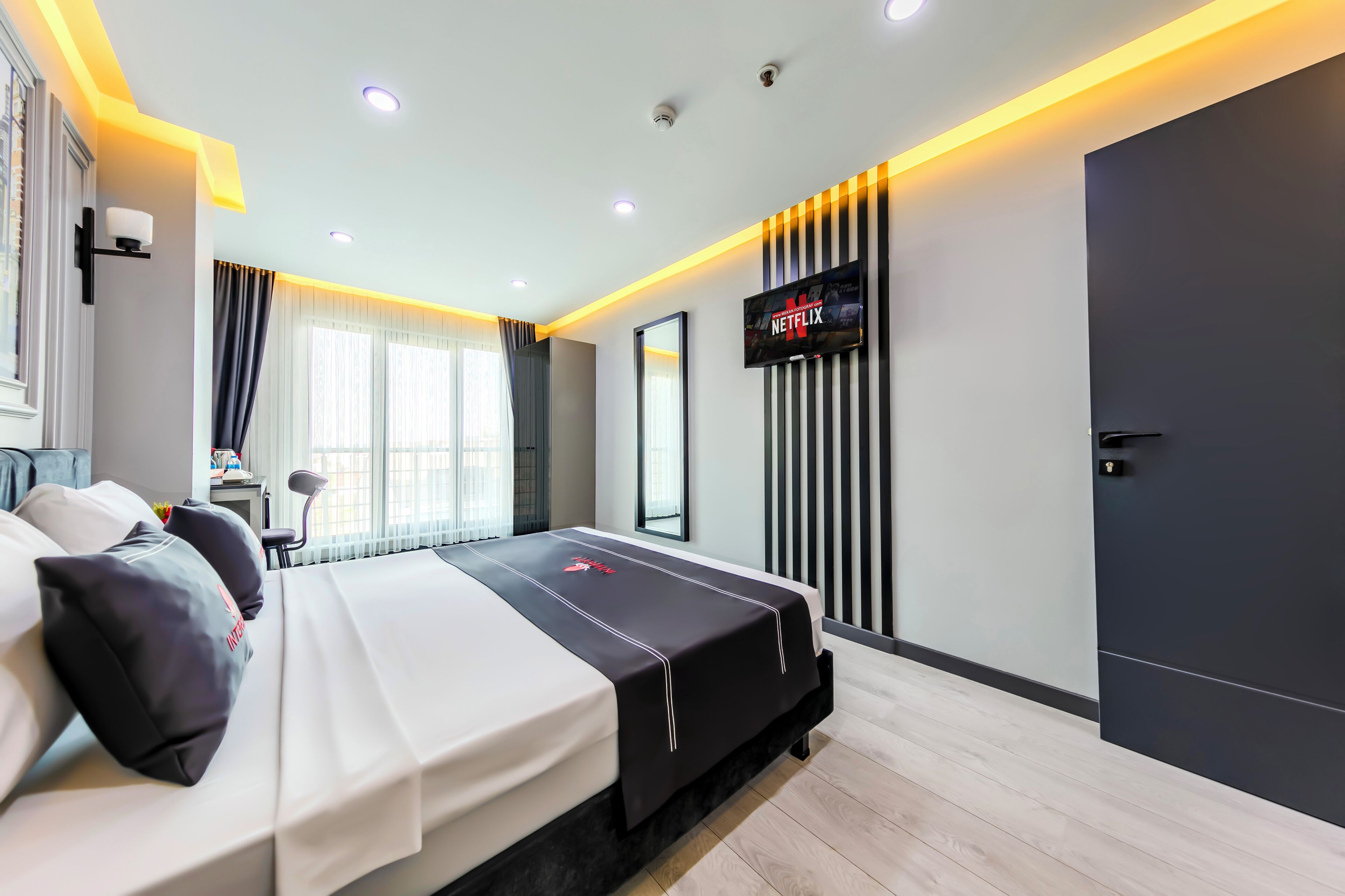 A modern hotel room with a large bed, a flat-screen TV mounted on the wall, and a door with a handle.