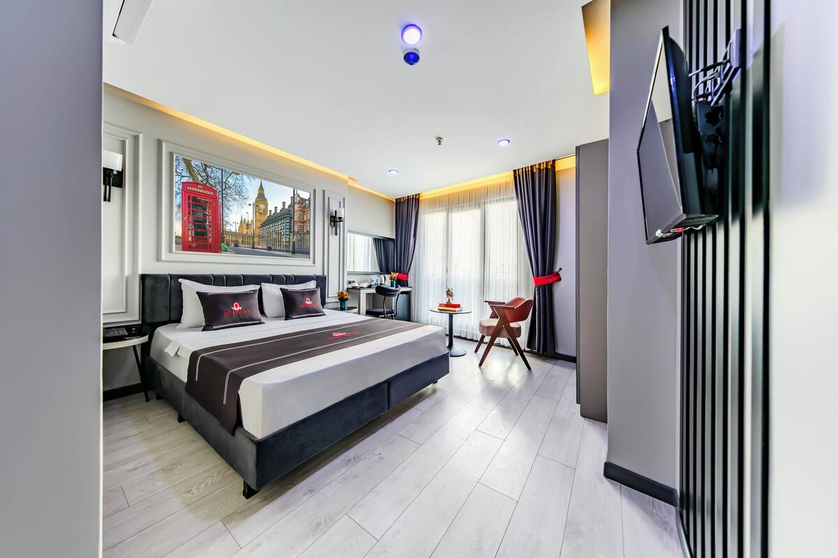 A modern hotel room with a large bed, a desk, a chair, and a TV mounted on the wall.