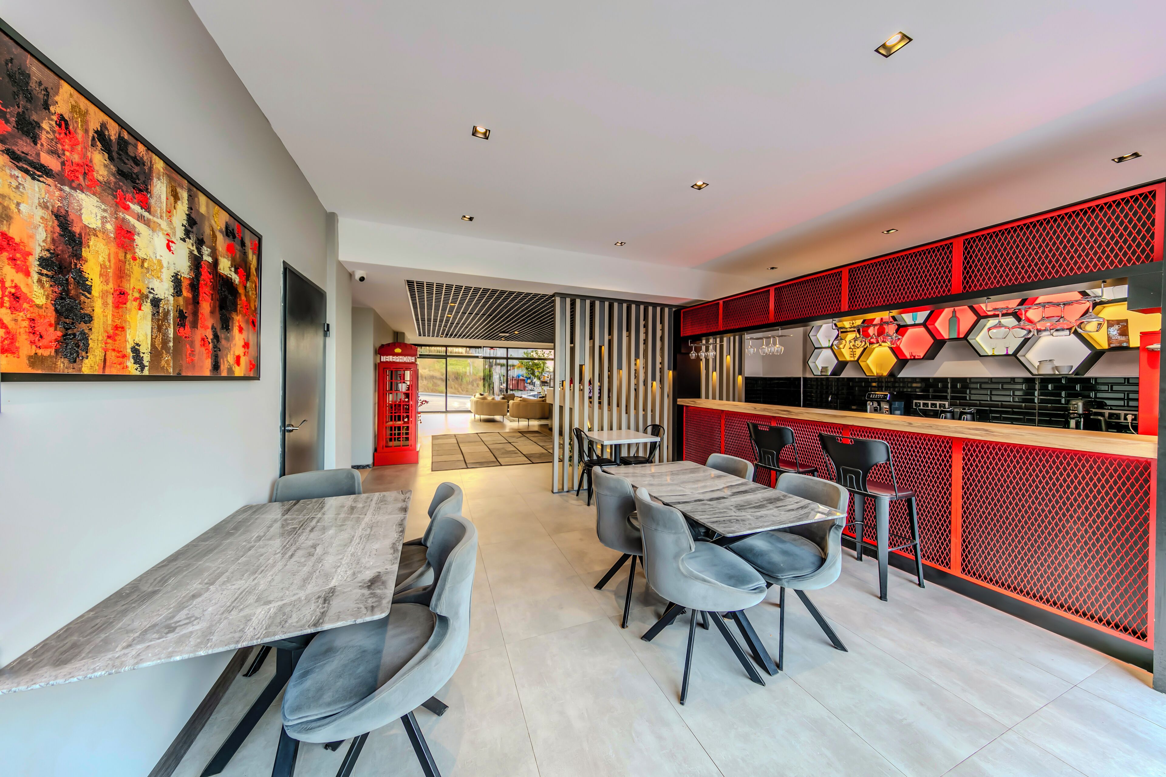 Un'area ristorazione moderna con un grande dipinto astratto, una zona bar con lampade esagonali e vista sull'esterno.