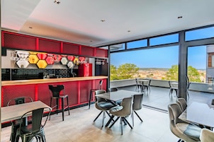 Un comedor moderno con una pared de acento roja, lámparas hexagonales y vistas de la ciudad a través de amplias ventanas.
