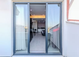 Un apartamento moderno con puerta de vidrio corredera que da a un balcón, una kitchenette, zona de comedor y un dormitorio.