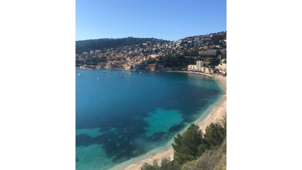 Une ville côtière bordée d’une mer d’un bleu profond, d’une plage de sable et de bâtiments qui s’alignent le long du rivage.