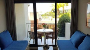Une pièce avec deux canapés bleus, une petite table blanche ornée d’un vase, et une vue sur un balcon avec une table et des chaises.