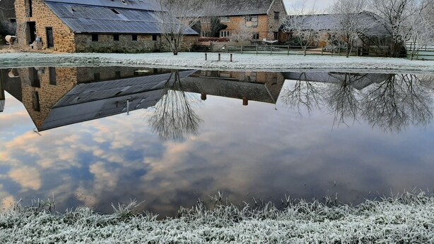A stone building with a sloped roof and solar panels, reflecting in a calm body of water. - Romantic getaway (Donyatt)