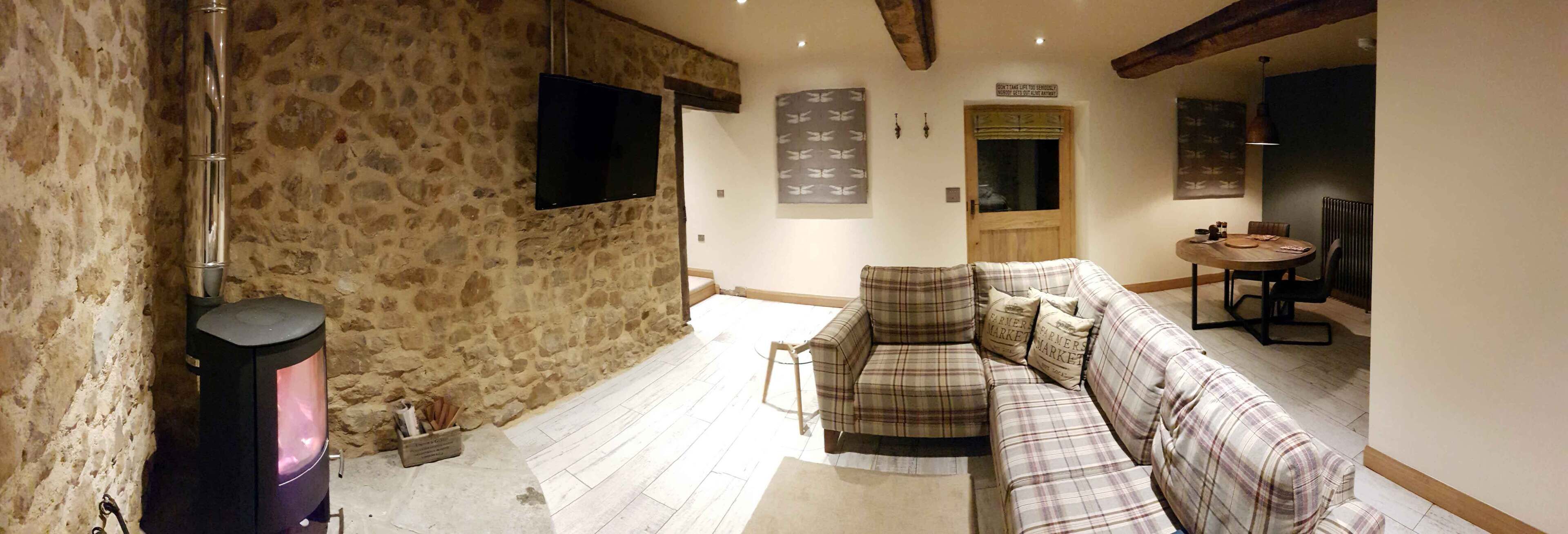 Un interior rústico con pared de piedra, chimenea, sofá de cuadros y puerta de madera.