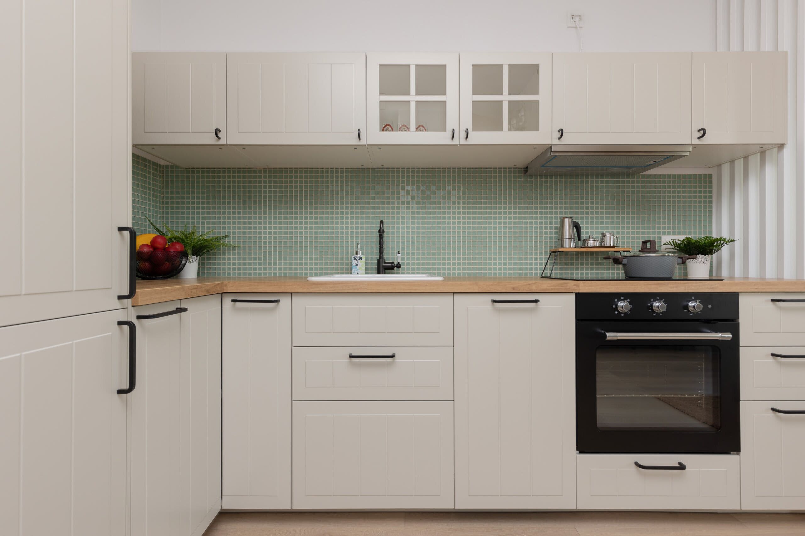 Una cocina moderna con armarios blancos, un horno negro y un salpicadero de azulejos verdes.