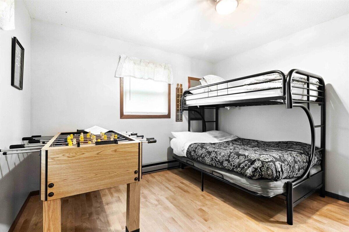 A compact room with a bunk bed, a wooden foosball table, and a window with a white valance.