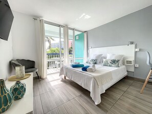 Une chambre d’hôtel moderne dotée d’un grand lit, d’un balcon avec vue et d’un coin salon comprenant un fauteuil et des vases décoratifs.