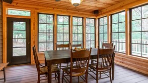 Un comedor de madera con una mesa y sillas, ventanas amplias y un ventilador de techo.