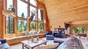 A cozy cabin interior with a large window, wooden walls, a sofa, a coffee table, and a television. - Charming Duck Creek Village Cabin | Fireplace (Duck Creek Village)