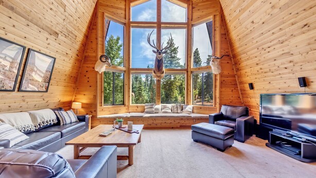 A log cabin interior with a large window, a sofa, a coffee table, and a TV. - Charming Duck Creek Village Cabin | Fireplace (Duck Creek Village)