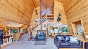 A wooden cabin interior with a staircase, a fireplace, a sofa, and a dining area. - Charming Duck Creek Village Cabin | Fireplace (Duck Creek Village)