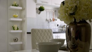 A kitchen with white shelves, a white chair, and a vase with flowers. - The Roost Group - 1 Bedroom - Ground (Gravesend)
