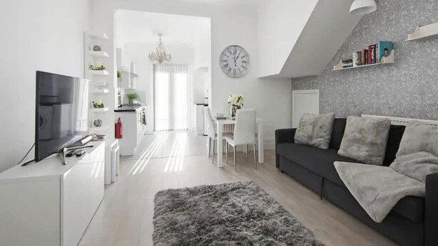 A modern living room with a sofa, TV, and a dining area with chairs and a table. - The Roost Group - 1 Bedroom - Ground (Gravesend)