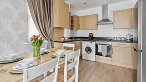 A modern kitchen with wooden cabinets, a washing machine, and a dining area with a table set for two.