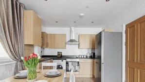 A compact kitchen with wooden cabinets, a washing machine, a coffee maker, and a refrigerator.