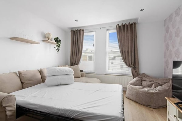 A bedroom with a bed, a sofa, a bean bag, a TV, and a window with curtains.