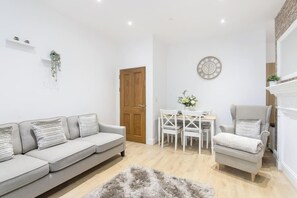 A living room with a sofa, armchair, dining table, and chairs.