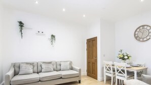 Una sala moderna con un sofá, una mesa de comedor, sillas, una puerta de madera y plantas en la pared.