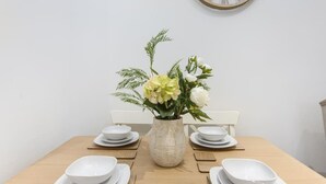 Una mesa de comedor con platos blancos, un jarrón con flores y un reloj de pared.