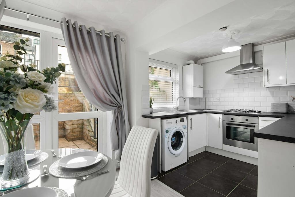 A modern kitchen with a washing machine, oven, and a dining area with a table set for two.