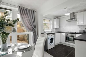 A modern kitchen with a washing machine, oven, and a dining area with a table set for two.