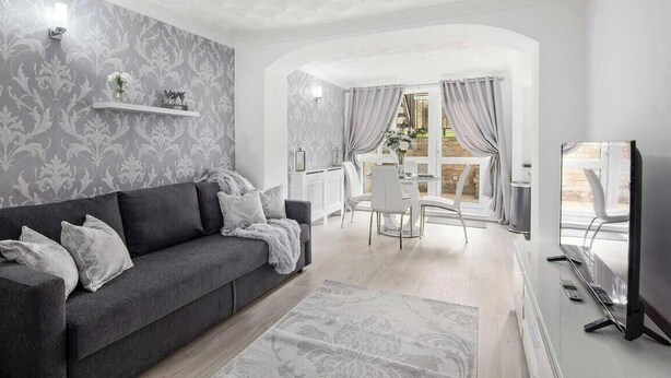 Un salon moderne avec un canapé gris, un téléviseur à écran plat et un coin repas comprenant une table et des chaises.