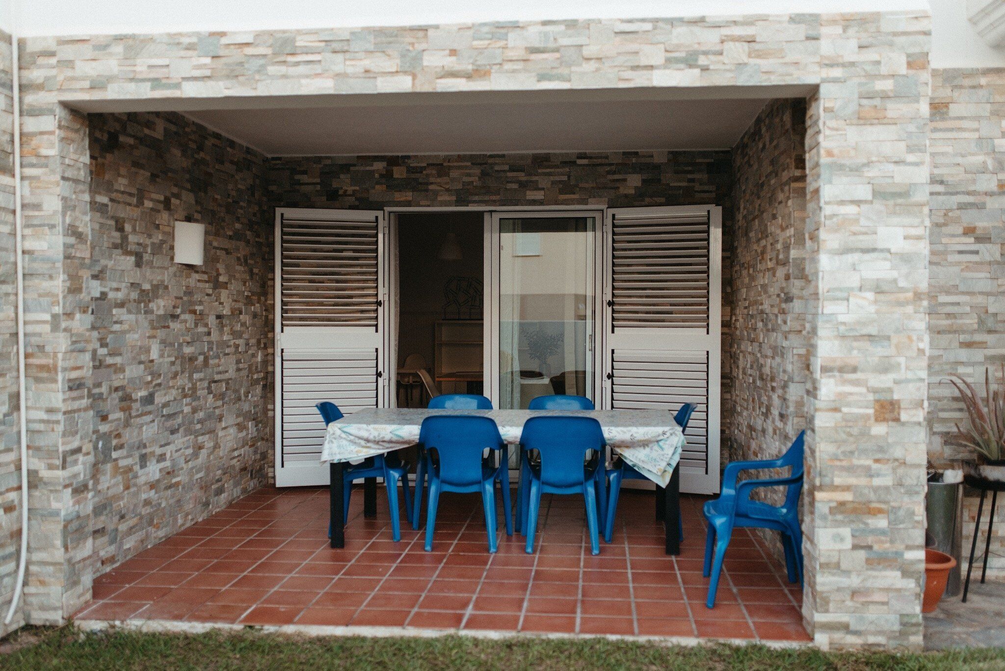 An outdoor patio with a table and chairs, a tiled floor, and a stone wall.