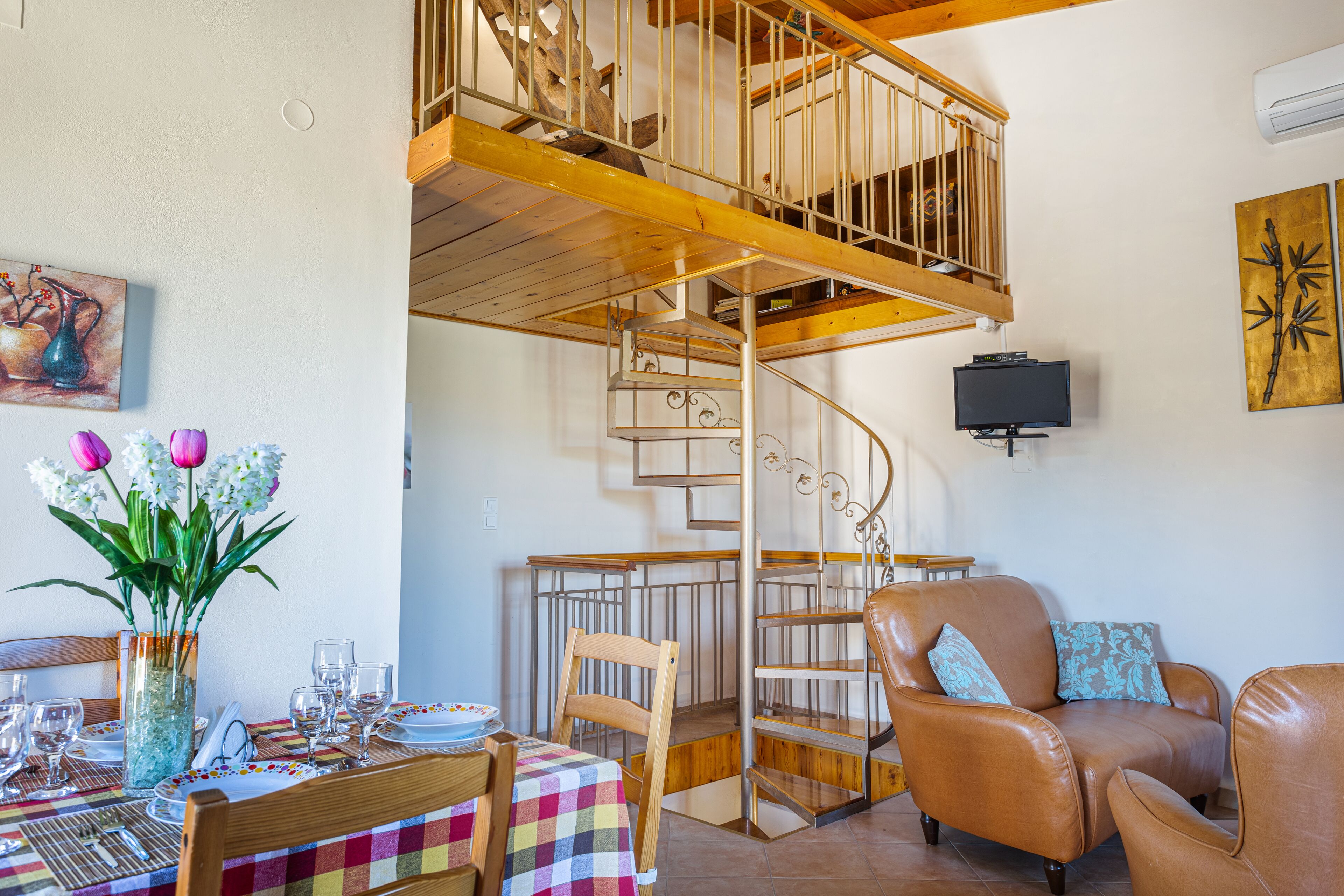A dining area with a wooden table set for a meal, a spiral staircase, and a leather armchair.