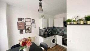 Een moderne keuken met witte kastjes, een zwart aanrecht en een ingebouwde wasmachine. Er staat een eettafel met stoelen en een vaas met bloemen.