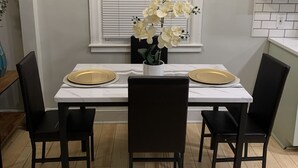 A dining area with a white table, black chairs, and a vase of white flowers. - Be our guest BOHO 2.0 (Charlotte)